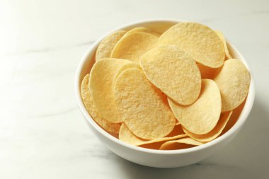 Lezzetli patates cipsleri beyaz mermer masada, yakın plan.