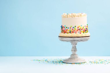 Açık mavi masaya renkli şekerlemeler serpiştirilmiş nefis bento keki, metin için yer.