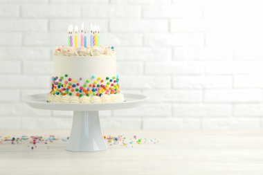 Renkli serpilmiş nefis bento keki ve beyaz tuğla duvara karşı açık ahşap masada yanan mumlar. Metin için boşluk