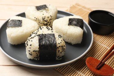 Rice balls (onigiri), soy sauce and chopsticks on wooden table, closeup. Traditional Japanese dish