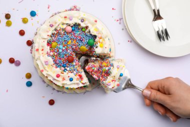 Beyaz arka planda renkli serpiştirilmiş nefis bento pastasından bir parça alan bir kadın.