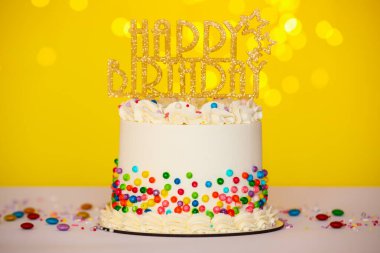 Renkli süslemeli lezzetli bento keki ve masasının üstünde sarı arka plan, bokeh etkisi.