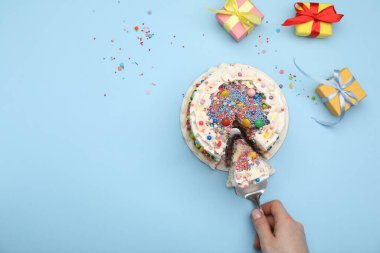 Açık mavi arka planda renkli serpiştirilmiş nefis bento pastasından bir parça alan bir kadın. Metin için boşluk