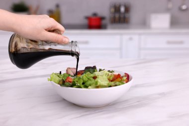 Mutfaktaki beyaz mermer masada lezzetli salataya balzamik sirke döken kadın, yakın plan.