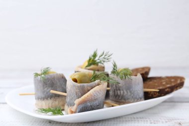 Zeytinli lezzetli ringa dürümleri, beyaz ahşap masada dereotu ve ekmek, yakın plan.