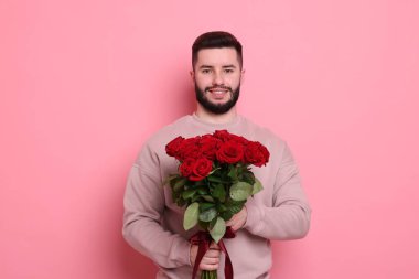 Pembe arka planda kırmızı güller açan mutlu bir adam.