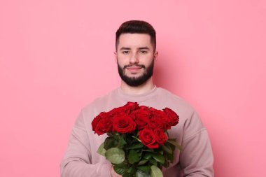 Pembe arka planda kırmızı gül buketi olan adam.
