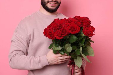 Pembe arka planda kırmızı gül buketi olan adam, yakın plan.