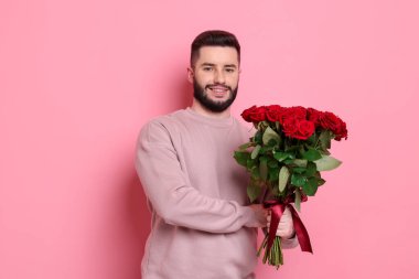Pembe arka planda kırmızı güller açan mutlu bir adam.