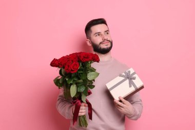 Kırmızı gül buketi ve pembe arka planda hediye kutusu olan bir adam.