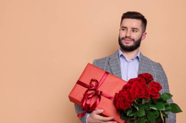 Kırmızı gül buketi ve bej arka planda hediye kutusu olan mutlu adam, mesaj için yer var.