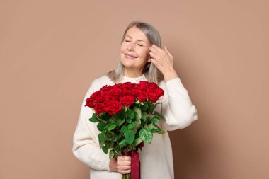 Bej arka planda bir buket gülle gülümseyen kadın.
