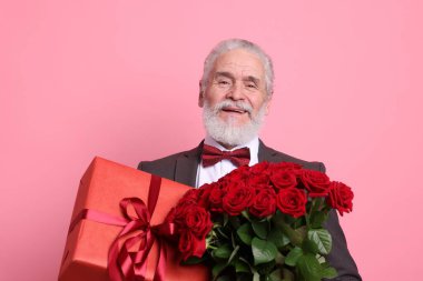 Kırmızı gül buketi ve pembe arka planda hediye kutusu olan son sınıf öğrencisi.