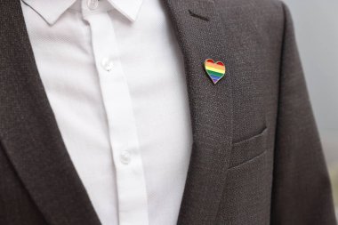 Kapalı alanda LGBT bayrağı renginde kalp şeklinde iğnesi olan adam, yakın plan