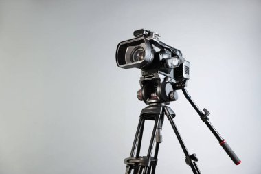 Açık gri arkaplanda tripodu olan modern video kamera, metin için boşluk