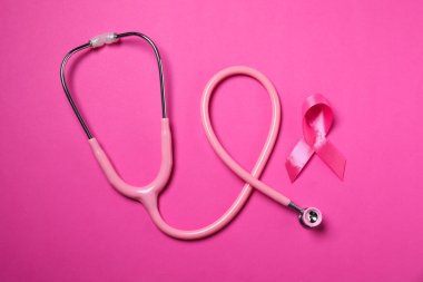 Göğüs kanseri farkındalığı. Renk arkaplanı üzerine pembe kurdele ve steteskop, üst görünüm