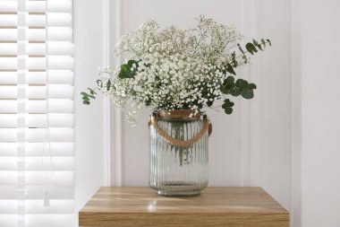 Beautiful gypsophila flowers and eucalyptus branches in vase on table at home