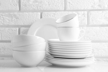 Different clean dishware on white table near brick wall