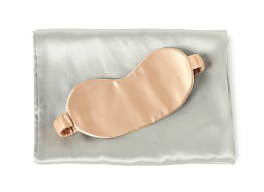 Beyaz arka planda ipek çarşaflar ve uyku maskesi, üst manzara.