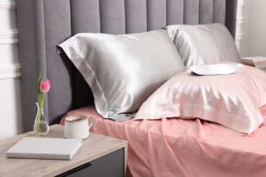 İçinde güzel ipek çarşaflar, uyku maskesi ve komodin olan bir yatak.