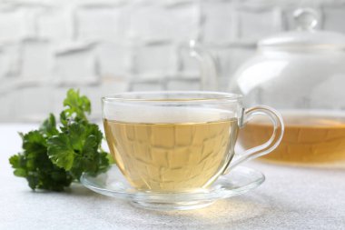 Cam bardakta Aromatik bitki çayı, taze maydanoz ve açık gri masada çaydanlık, yakın plan.
