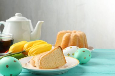 Lezzetli kek parçaları, Paskalya yumurtaları, laleler ve çay açık mavi ahşap masada.