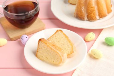 Lezzetli kek parçaları, pembe ahşap masada paskalya yumurtası ve çay, yakın plan.