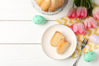 Lezzetli kek parçaları, beyaz ahşap masada paskalya yumurtası ve laleler, düz yatak. Metin için boşluk