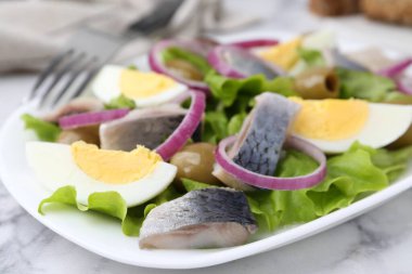 Ringa balıklı lezzetli salata, yumurta ve sebzeler beyaz mermer masada, yakın plan.