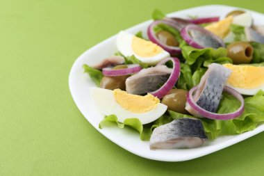 Ringa balıklı lezzetli salata, yeşil arka planda yumurta ve sebze, yakın plan. Metin için boşluk
