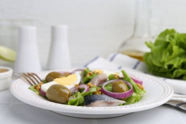 Ringa balıklı lezzetli salata, yumurta, hardal ve sebzeler beyaz fayanslı masada, yakın plan.