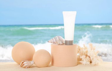 Okyanusun yakınındaki kumlu sahilde güneş kremi tüpü. Geometrik şekiller ve deniz kabukları ile şık bir sunum