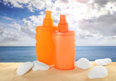 Deniz kenarındaki kumlu sahilde güneş kremi ve taşlar.