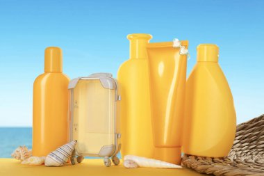 Güneş kremi ürünleri, oyuncak bavul ve okyanus kenarındaki masada deniz kabukları.