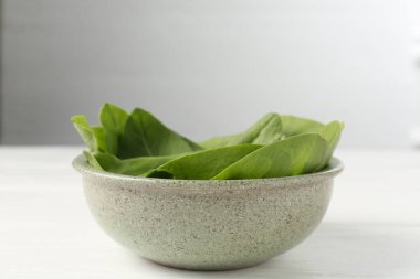 Taze yeşil kuş yaprakları kasede beyaz ahşap masada, yakın plan.