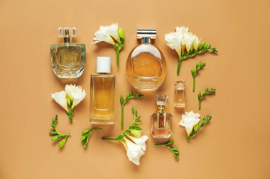 Düz kompozisyonda aromatik parfüm şişeleri ve bej arka planda güzel çiçekler vardı.