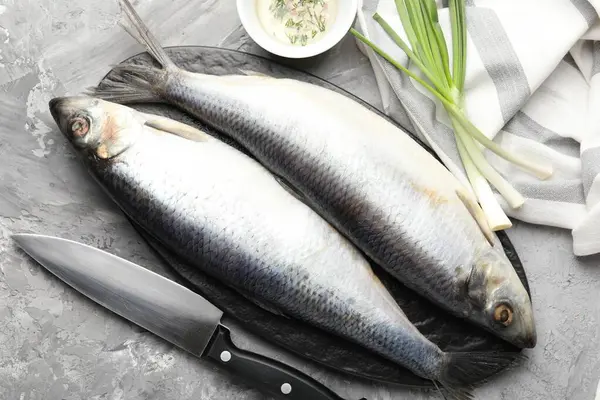 Tuzlu ringa balıkları, baharatlar ve bıçak gri masada, düz yerde.