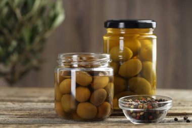 Cam kavanozlarda turşulu zeytin ve ahşap masada baharatlar, yakın plan.