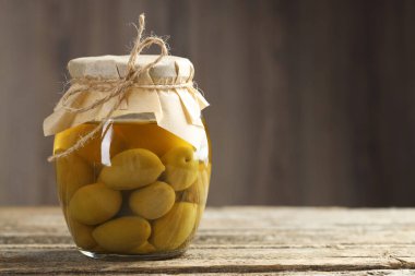 Ahşap masada cam kavanozda yeşil zeytin turşusu, yakın plan. Metin için boşluk