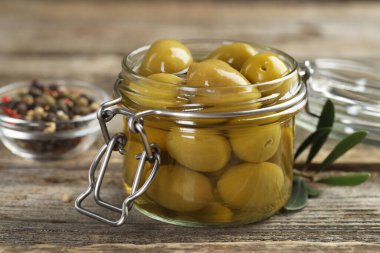 Cam kavanozda turşulu yeşil zeytin ve ahşap masada baharatlar, yakın plan.