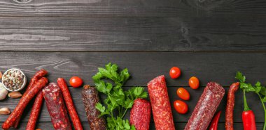 Farklı tütsülenmiş sosisler, domatesler, maydanoz ve biberli siyah ahşap masa, düz yatak. Metin için boşluk