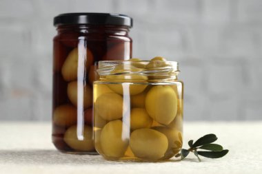 Kavanozlarda turşulu yeşil zeytin ve beyaz desenli masada yapraklar, yakın plan.