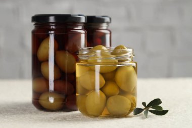 Kavanozlarda turşulu yeşil zeytin ve beyaz desenli masada yapraklar, yakın plan.