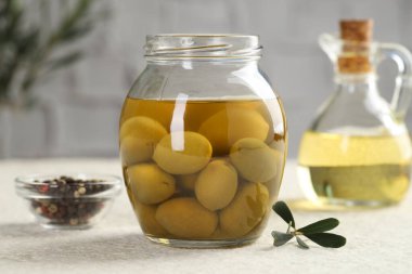 Kavanozda turşulu yeşil zeytin, beyaz desenli masada yağlı ve biberli mısır, yakın plan.