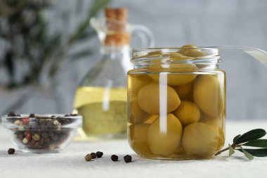 Kavanozda, çatalda, yağda ve biberli yeşil zeytinleri beyaz desenli masada, yakın plan.