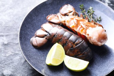 Çiğ ıstakoz kuyruğu, kireç ve kekik karanlık masada, yakın plan.