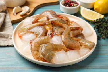 Taze çiğ karidesler, buz küpleri ve baharatlar açık mavi ahşap masada, yakın plan.