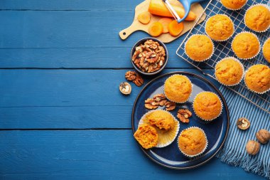 Lezzetli havuçlu kekler, cevizler ve taze sebzeler mavi ahşap masada, düz uzanmış. Metin için boşluk