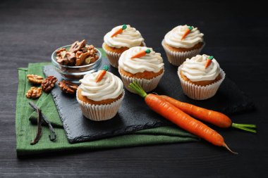 Kremalı havuçlu kekler, cevizler ve taze sebzeler siyah ahşap masada, yakın plan.