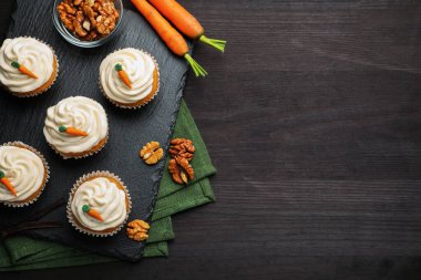 Kremalı havuçlu kekler, cevizler ve taze sebzeler siyah ahşap masada, düz bir şekilde. Metin için boşluk